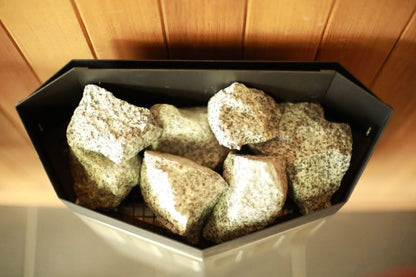 Sauna stones packed into a heater tray under a cedar ceiling